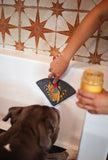 Dog in bath with lick mat ssuctioned to the tub with peanut butter spread.