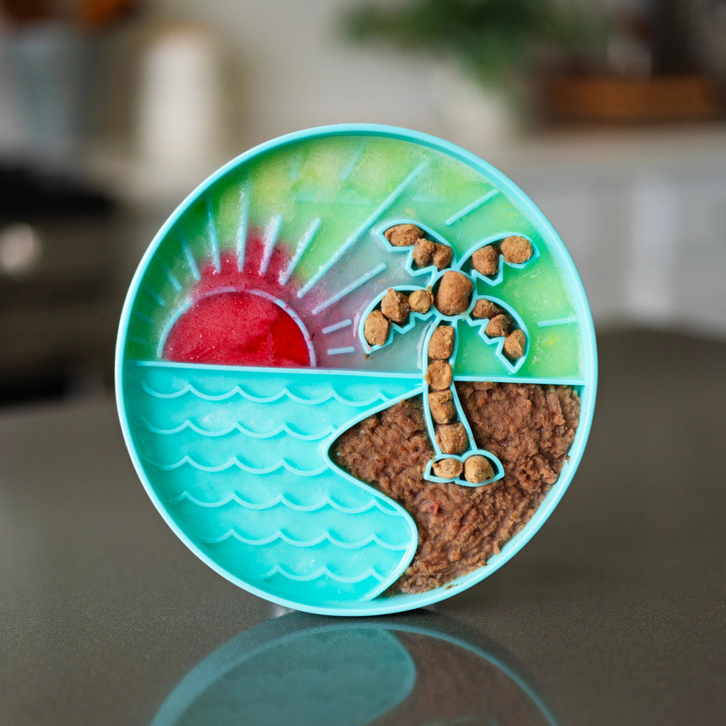 Teal silicone dog bowl with beach and sunset theme stuffed with raw dog food and kibble.